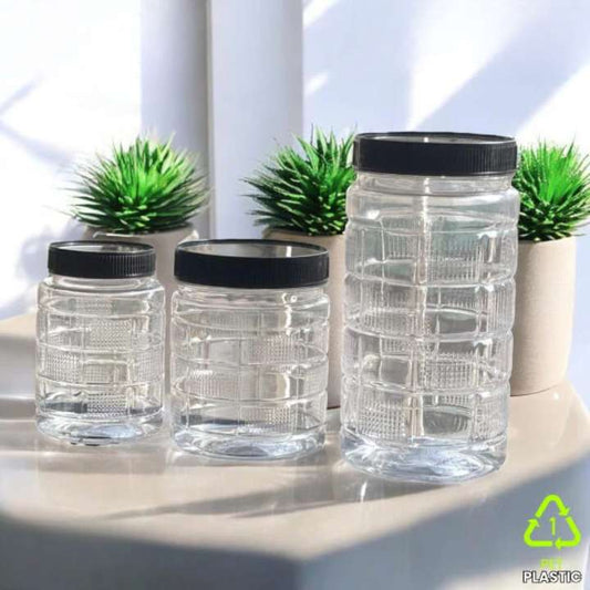 Set of clear jars with black lids on a light surface with plants in the background