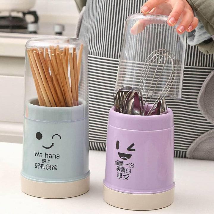 Two cylindrical containers with cartoon faces, one holding wooden sticks and the other with utensils, on a white surface.