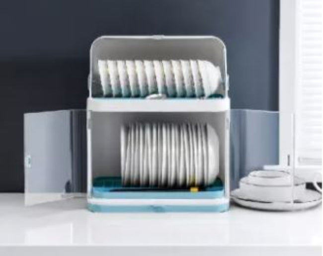 Closed transparent plastic dish drying rack and storage cabinet, shown on a kitchen countertop, neatly holding and covering bowls, plates, and cutlery inside the organized compartments.