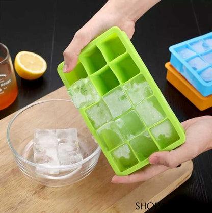 Green silicone ice cube tray with ice cubes, held by a hand, on a wooden surface with a glass of iced tea and lemon.
