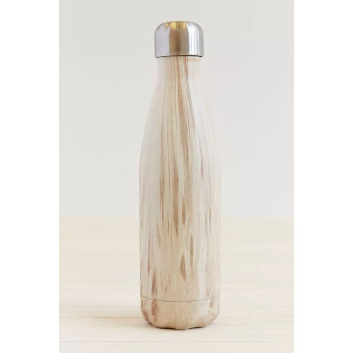 A reusable insulated bottle with a light natural wood grain finish and a brushed silver metal lid, standing on a light wood surface against a neutral off-white background.