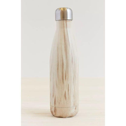 A reusable insulated bottle with a light natural wood grain finish and a brushed silver metal lid, standing on a light wood surface against a neutral off-white background.