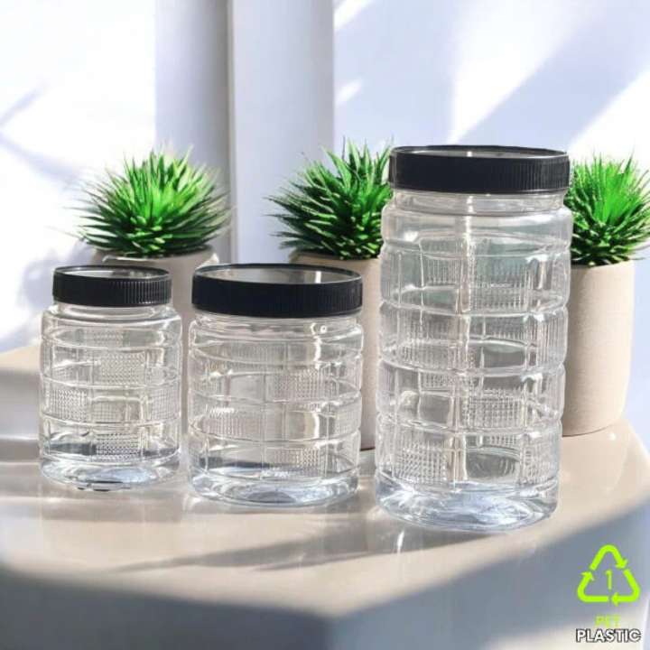 Set of clear jars with black lids on a light surface with plants in the background