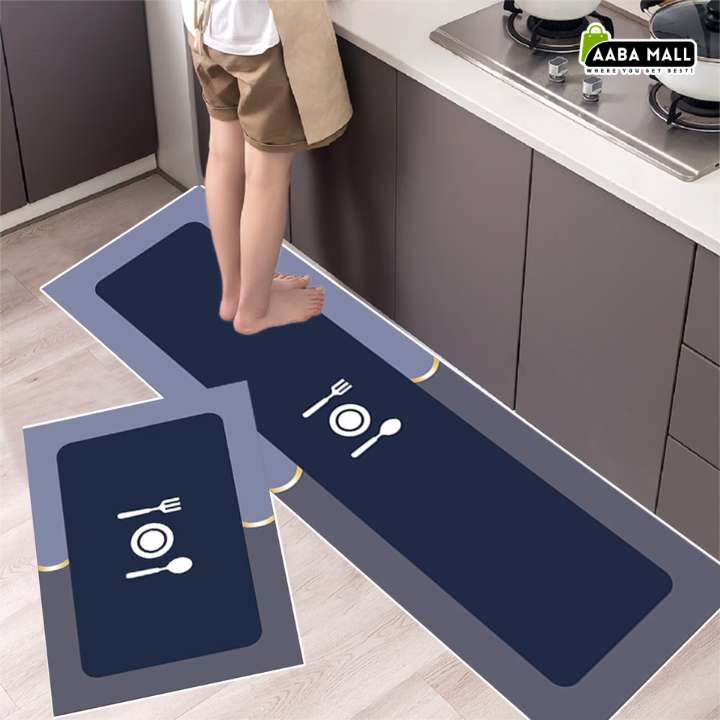 A rectangular kitchen mat with a dark navy blue center, gray border, and white table setting icon, shown in a kitchen with a child stepping on it. A smaller matching mat is displayed in the foreground, and an 'AABA MALL' logo appears in the top right corner.