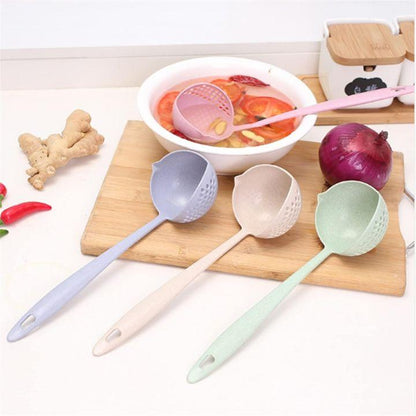 Three plastic kitchen ladles in pastel blue, beige, and mint green are arranged on a wooden cutting board with a bowl of soup, an onion, ginger, and chili peppers around them.