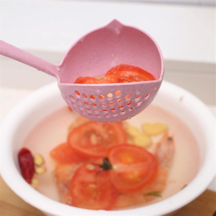 A pink plastic slotted ladle holding sliced red tomatoes above a white bowl of water with ingredients, shown in a kitchen-like setting.