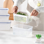Set of three stackable fridge storage containers with green, blue, and clear lids, showing inner detachable drain basket with fresh berries and vegetables.