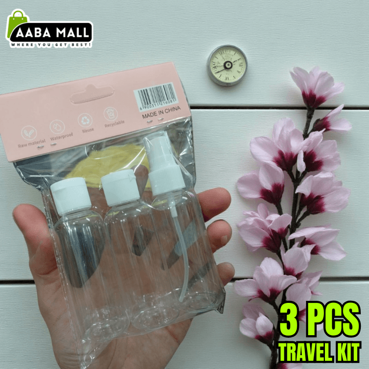 Hand holding a travel kit with three bottles and packaging, next to pink flowers on a light wooden surface.