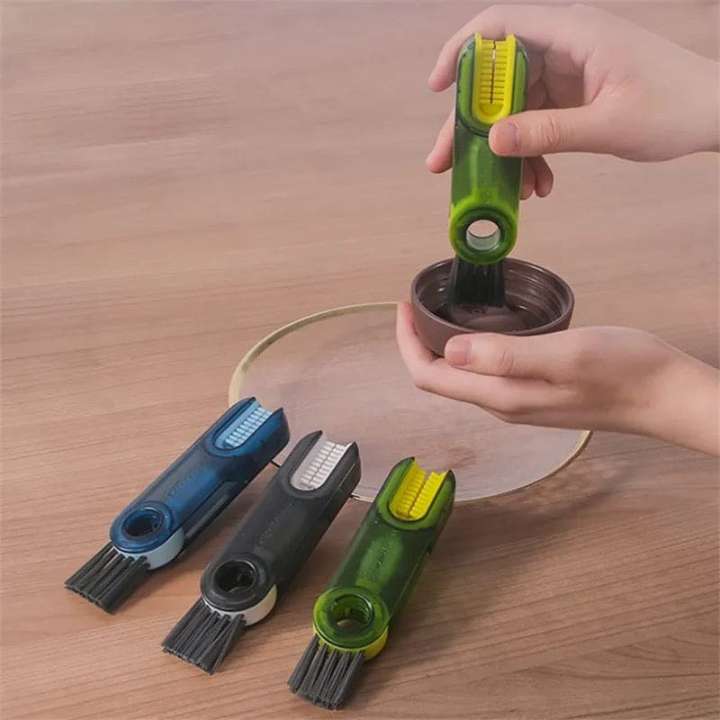 Hand using a green tool to clean a pot on a wooden surface with other tools in the foreground.