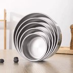 Set of metal baking pans stacked on a wooden surface with a white background