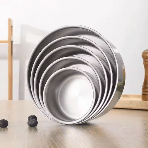 Set of metal baking pans stacked on a wooden surface with a white background