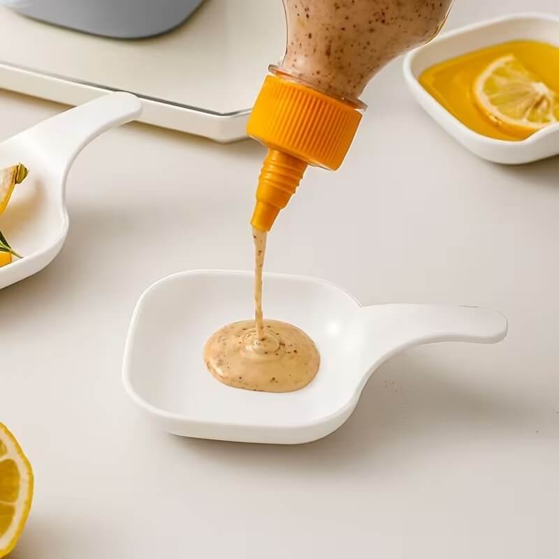 Squeeze bottle pouring a sauce into a white dish on a light surface.