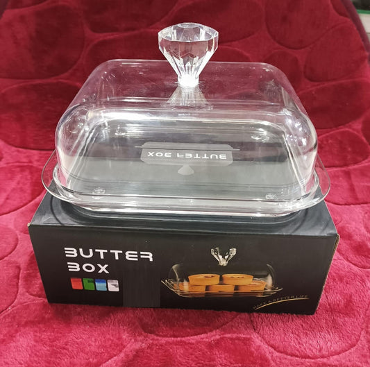 An acrylic butter dish with a plastic lid and knob, displayed on a red surface, with the product packaging visible in the background.