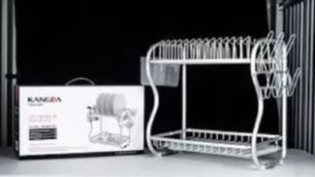 A silver 2-tier aluminum dish drying rack with a utensil holder and black drip tray, fully loaded with plates and bowls on a kitchen countertop.