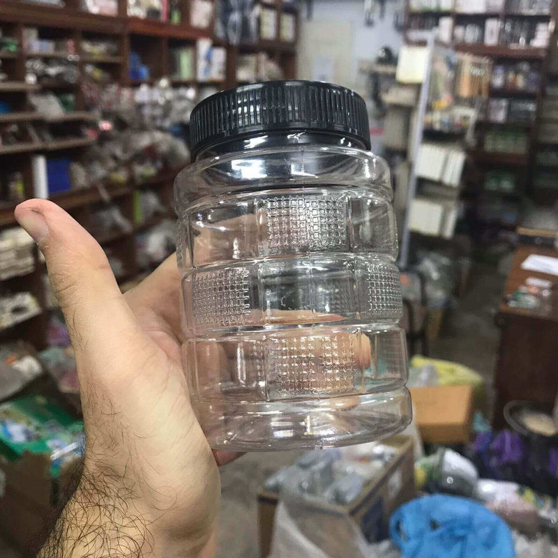 Clear plastic container with a black lid held in a hand against a store background