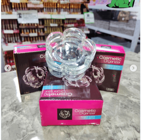 Clear glass cosmetic organizer on a pink box with 'Cosmetic Organizer' branding in a store setting.