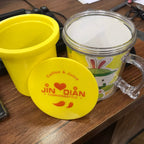 Yellow mug with a lid and clear mug with cartoon character on a wooden surface