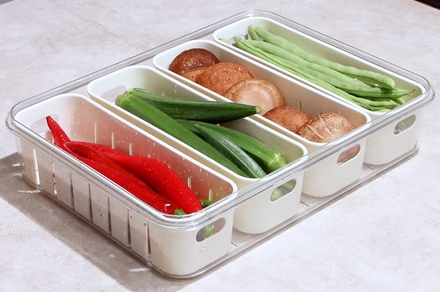 Divided food container with compartments of vegetables and mushrooms on a light background