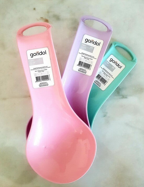 Three plastic measuring spoons in pink, purple, and teal, each with a white paper label showing the brand 'goñdol' and barcode, arranged on a light marble-like surface.