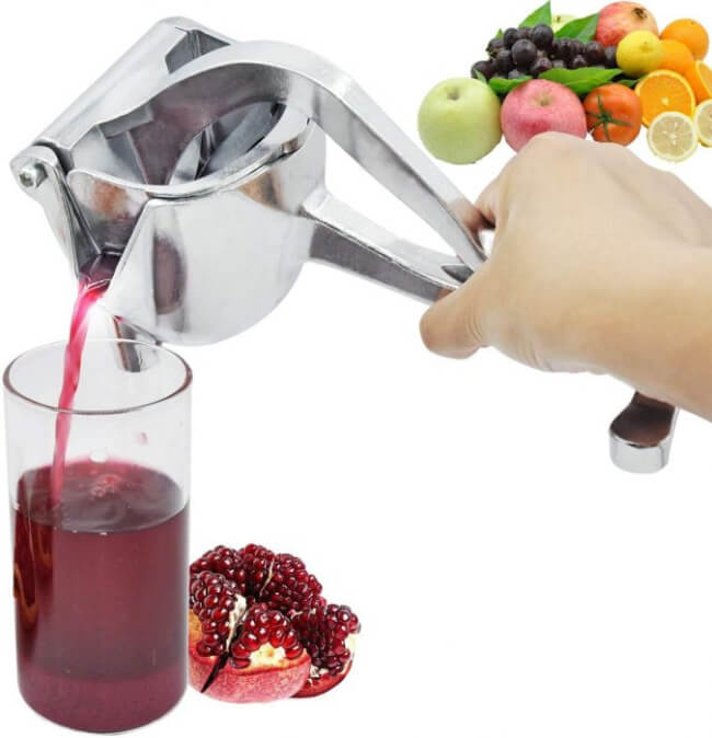 Hand using a manual juicer to extract juice from fruits and vegetables, with a glass of juice and pomegranate on a white background.