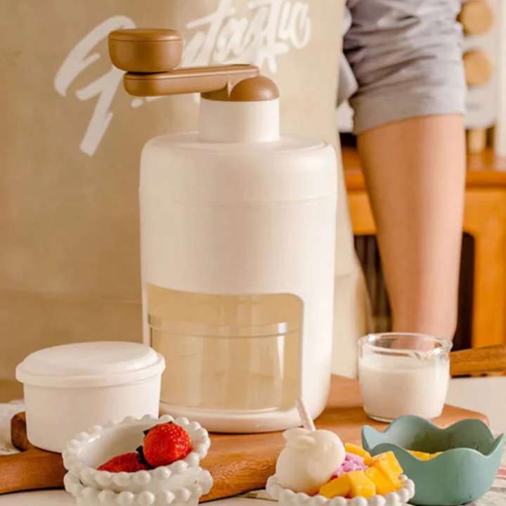 White and brown kitchen appliance on a counter with fruit and a glass of milk.