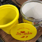 Yellow container with a lid featuring 'Jin Dian' branding on a wooden surface.
