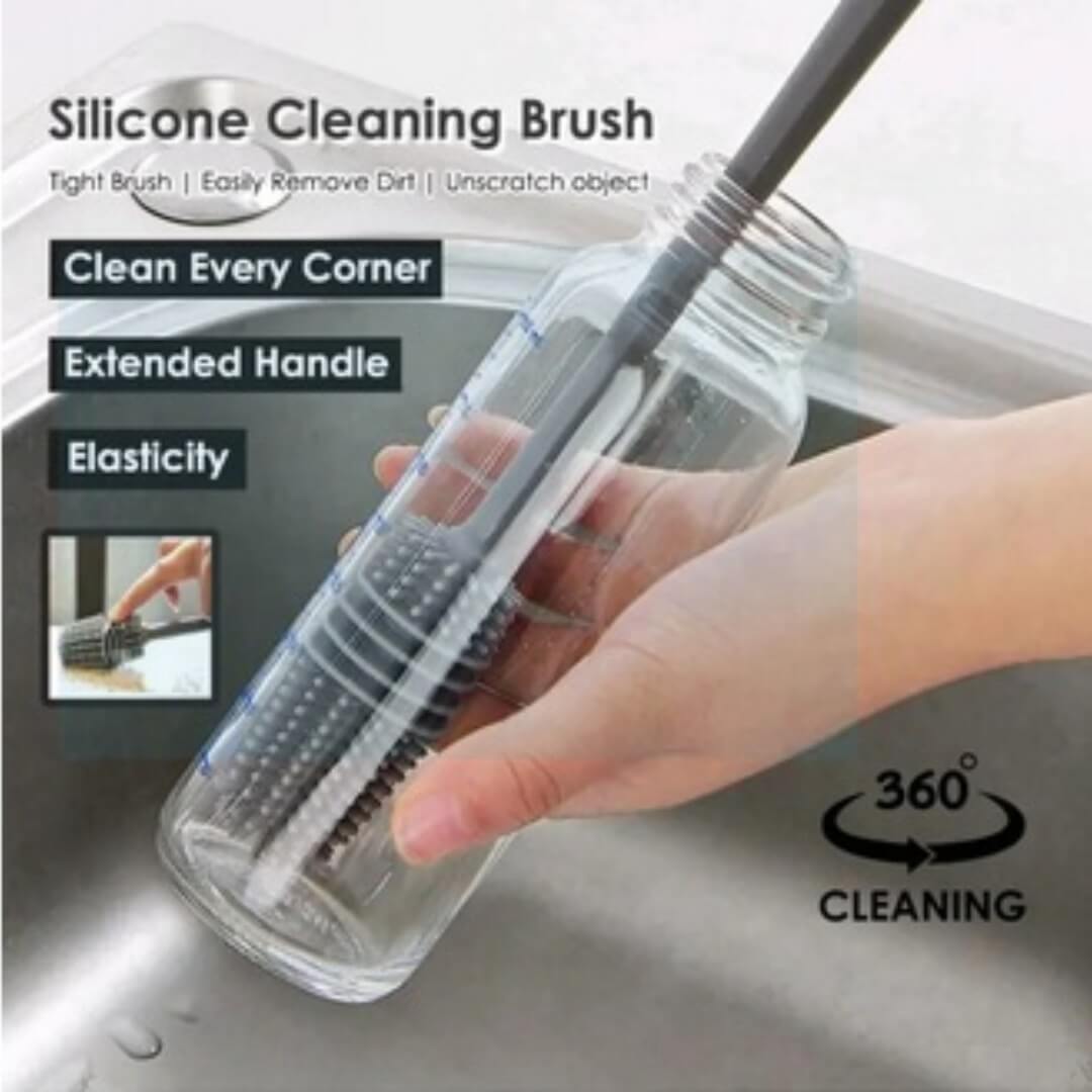 Silicone cleaning brush with clear handle and black bristles, held by a hand over a sink.
