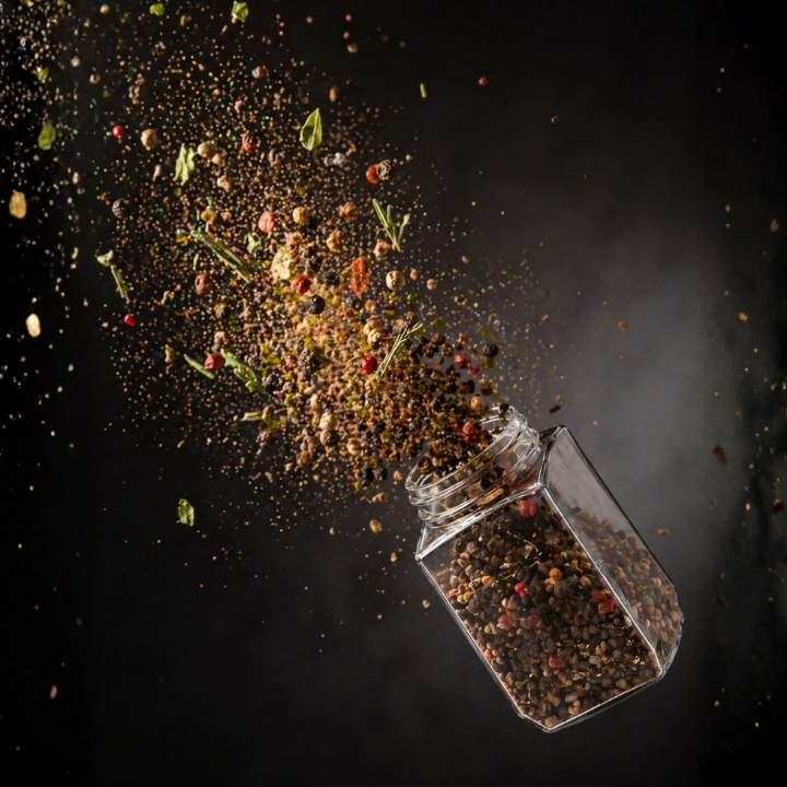 Spices spilling out of a glass container on a dark background