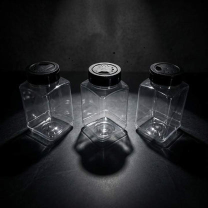 Three clear glass jars with black lids on a dark surface