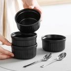 Set of black ramekins with ribbed interior on a light surface.