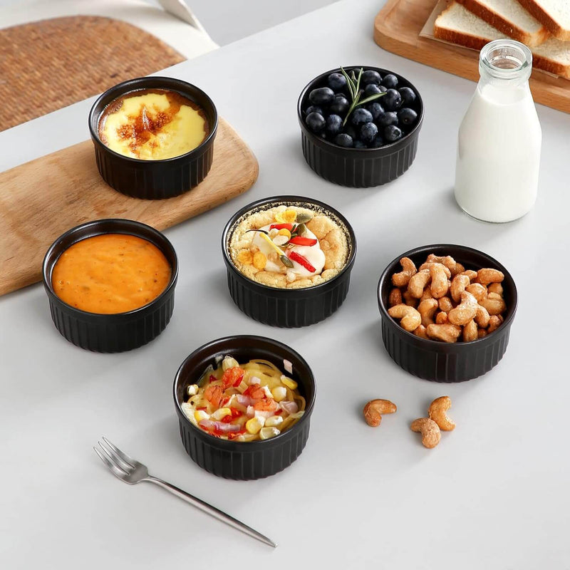 Assorted snacks in black ramekins on a white surface with a bottle of milk and bread in the background.