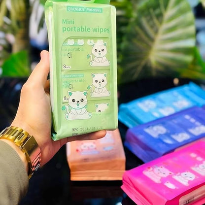 Hand holding a green package of mini portable wipes with cartoon cat design, against a blurred background.