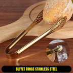 Gold buffet tongs on a wooden surface with bread and a glass of water.