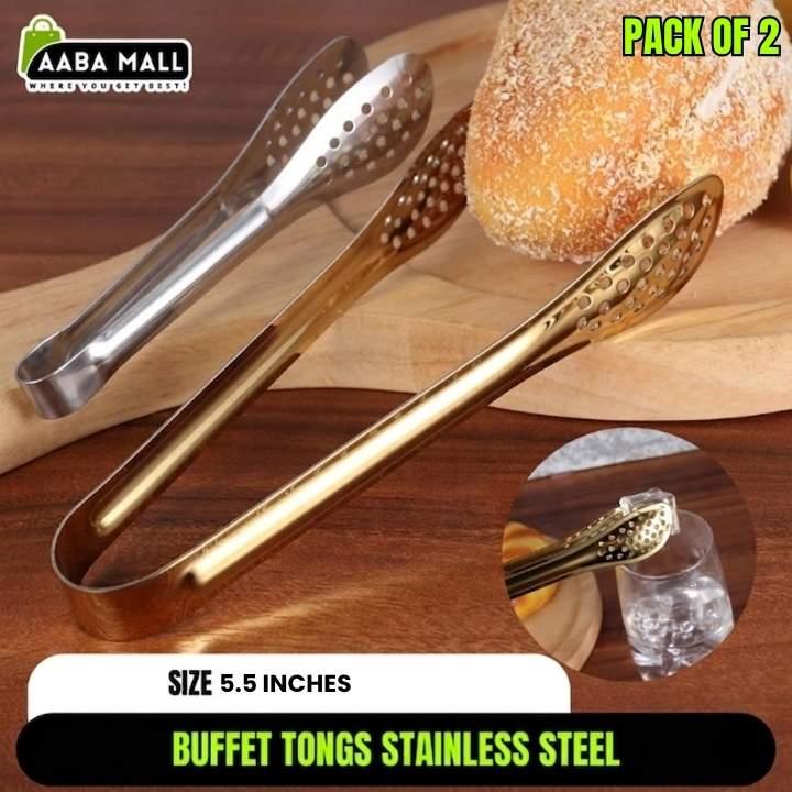 Gold and silver buffet tongs on a wooden surface with bread and a glass of water.