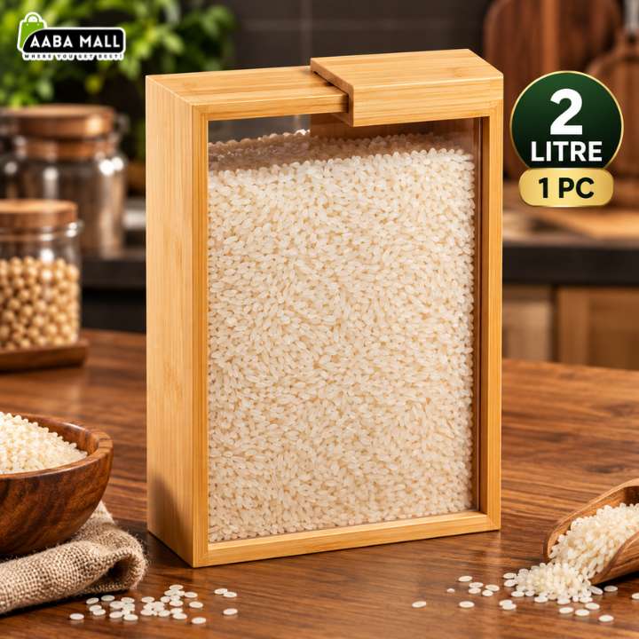 A rectangular bamboo-framed grain bin with a clear front panel filled with rice, shown on a wooden table with bowls of rice and jars in the background. A green circular badge reads '2 LITRE 1 PC', and an AABA MALL logo appears in the top left.