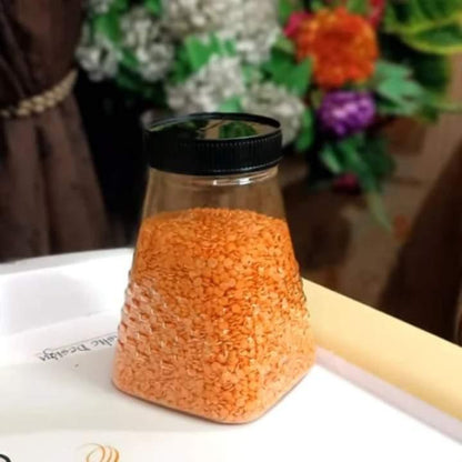 Clear container with orange contents on a white surface with a blurred floral background