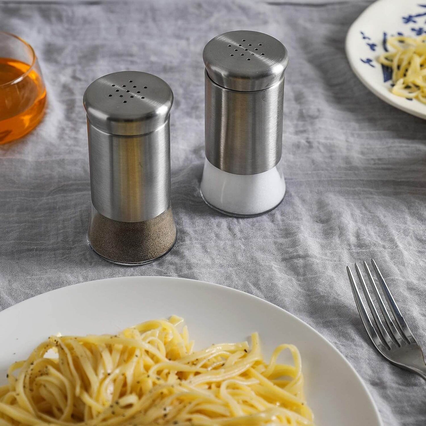 Two metal shakers on a table with pasta and a fork.