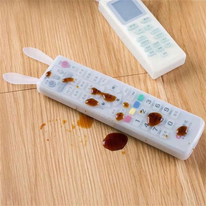 Remote control with a protective cover on a wooden surface, showing signs of spillage.