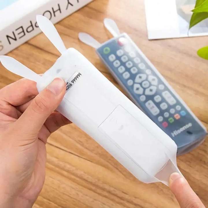 Hand holding a white remote control cover with a blurred remote control in the background.