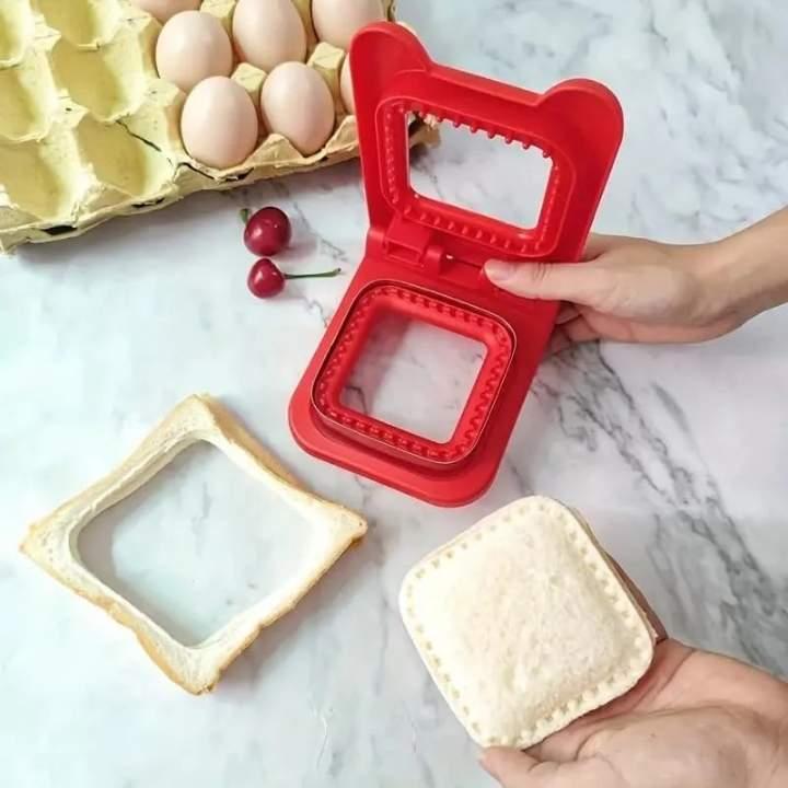Red square cookie cutter with two square cookies on a marble surface.
