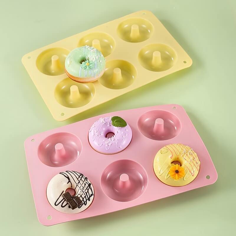 Two silicone donut molds, one yellow and one pink, with decorative donuts on a light green background.
