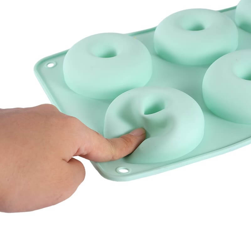 Silicone donut mold with a hand pressing one of the donut shapes.