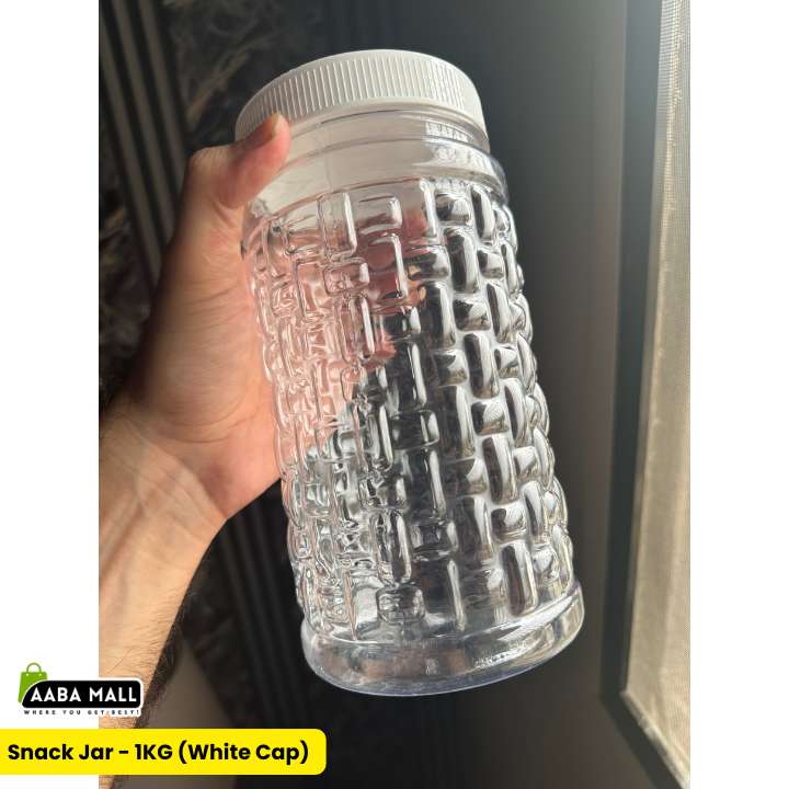 A hand holding a clear plastic snack jar with a textured pattern and a white ribbed cap, with text overlays indicating it is a 1KG white cap snack jar.