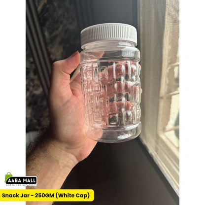 A hand holding a clear plastic snack jar with a ribbed embossed pattern and a white screw cap, positioned next to a window.