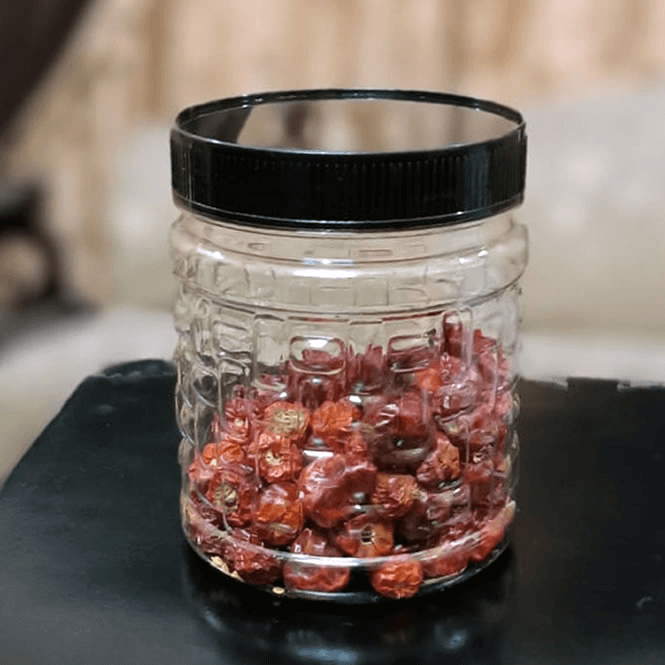 Clear premium plastic jar with black lid filled with red dried berries on a dark surface.