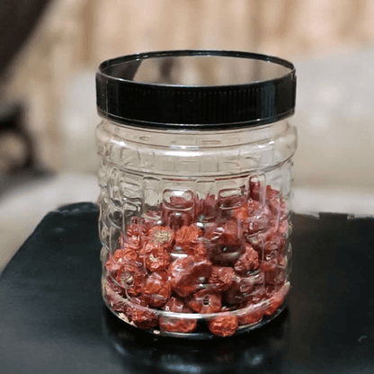 Clear premium plastic jar with black lid filled with red dried berries on a dark surface.