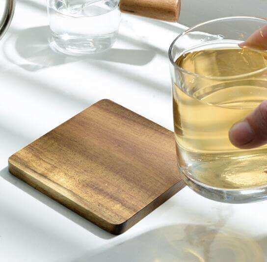 Wooden coaster on a white surface with a glass of liquid nearby
