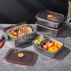 Set of stainless steel food containers with meals inside on a gray surface.