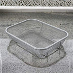 Metal wire laundry basket on a concrete surface with a white chair in the background