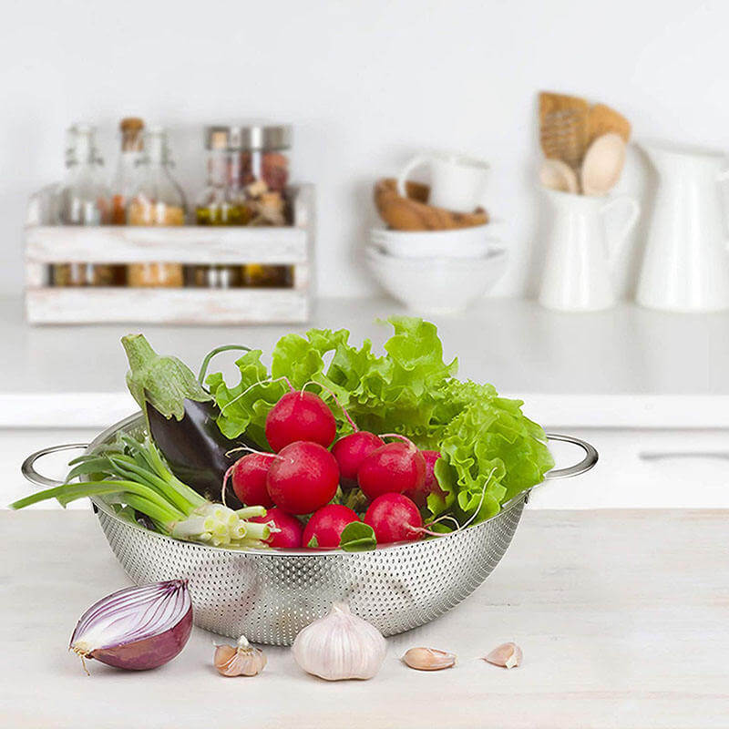 Colander with radishes, lettuce, and other vegetables on a kitchen counter.